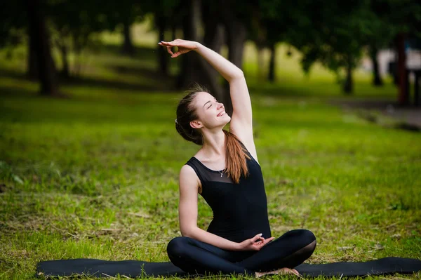 Vacker ung kvinna göra stretching motion på grönt gräs på park. Yoga träning — Stockfoto