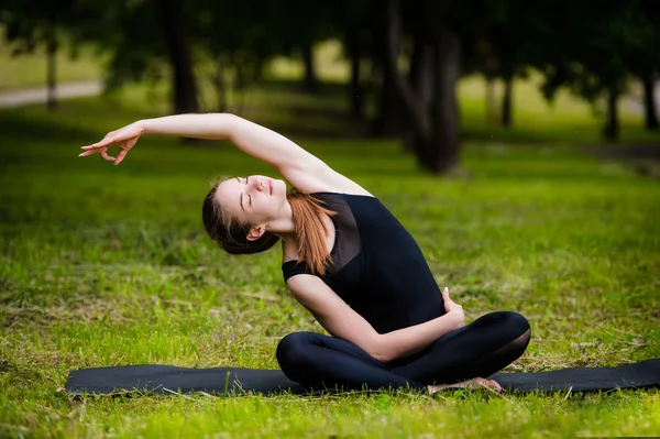 Vacker ung kvinna göra stretching motion på grönt gräs på park. Yoga träning — Stockfoto