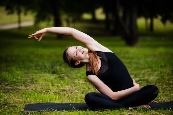 Lycklig, leende, ung kvinna vilar på gräset i parken efter yoga. Hon är klädd i mörka leggings. — Stockfoto