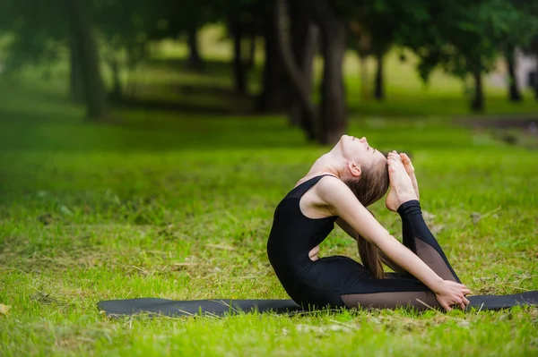 Ung kvinna gör gymnastik yoga och stretching i stadsparken på sunset — Stockfoto