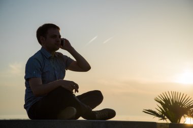 Telefondaki adam deniz plajının yanındaki bankta oturuyor.