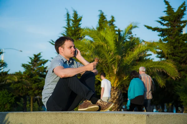 Jongeman op de promenade een ijsje eten en met behulp van zijn telefoon, misschien is hij één of wachten op iemand — Stockfoto