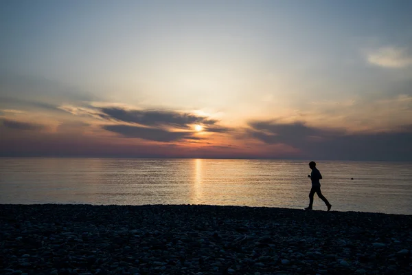 Silhouette de l'homme courant sur la plage au coucher du soleil — Photo