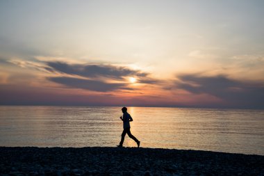 Çalışan ve busch günbatımı aşağıda kumsalda üzerinde egzersiz uzun boylu spor etkin adam silüeti.