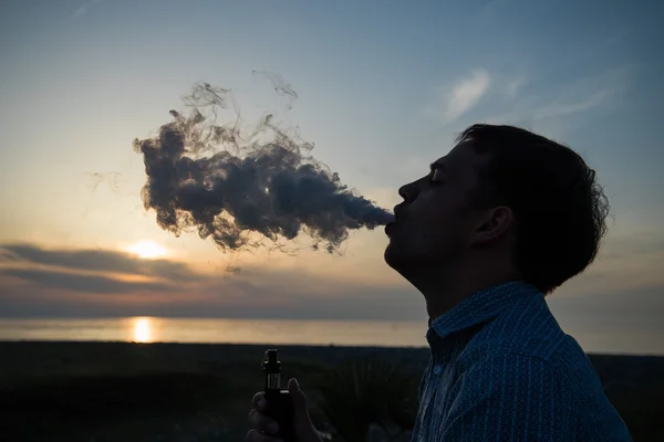 Man smoking vaping e-cigarette vape box mode over golden sunset — Stock Photo, Image
