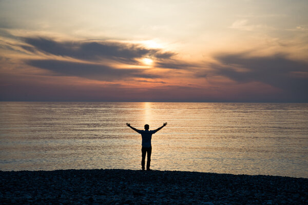 young man at sunset raises his hands up