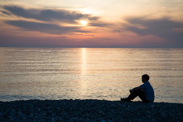 Man silhouette sitting on beach with sea and sunset background — Stock Photo, Image