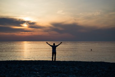Gün batımında deniz suyu yükseltilmiş kollarında bir adam silüeti