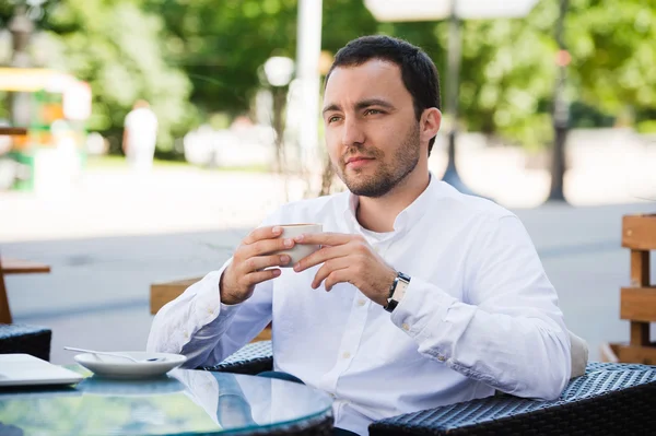 Уверенный в себе успешный бизнесмен в костюме наслаждаясь чашкой кофе во время обеденного перерыва на работе в современном ресторане, молодой умный человек или предприниматель расслабляется в открытом кафе глядя задумчиво — стоковое фото