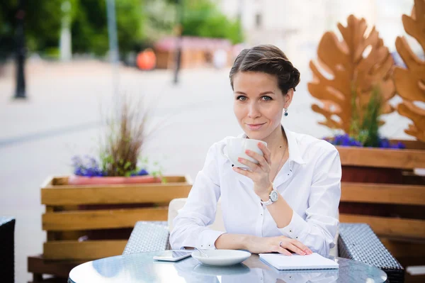 Descanso. Atractiva joven empresaria en ropa formal sonriendo mientras está sentada en la cafetería de la acera y bebiendo café . — Foto de Stock