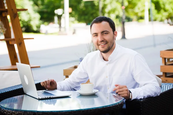 Beau homme d'affaires travaillant dans un café sur ordinateur portable, regardant vers la caméra et souriant — Photo