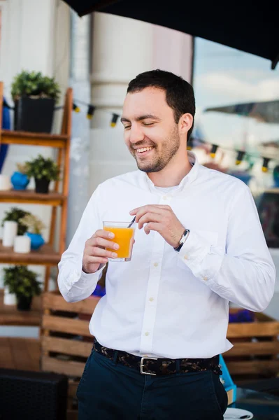 Красивый молодой человек держа стакан апельсинового свежего сока и улыбаясь, на открытом воздухе — стоковое фото