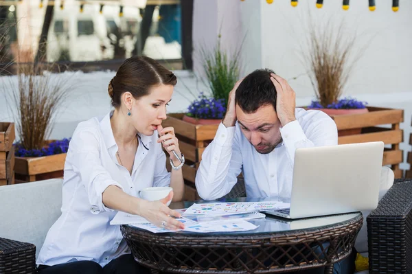 Mandlige og kvindelige forretningskolleger arbejder sammen om et hårdt problem på udendørs cafe. De har anstrengt udtryk på deres ansigter - Stock-foto
