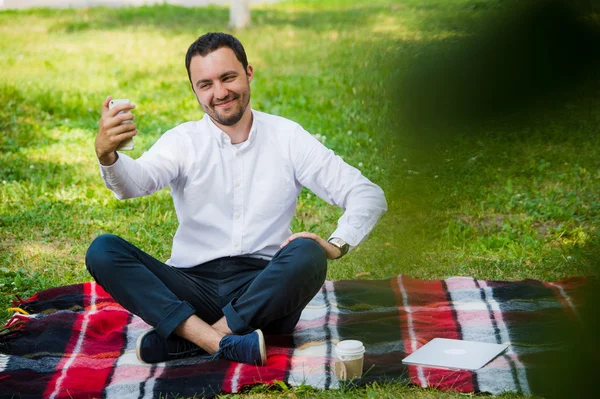 Foto van de knappe aardige vent buiten in de ochtend. Jonge man glimlachend en selfie foto op mobiele telefoon met cool expressies maken — Stockfoto