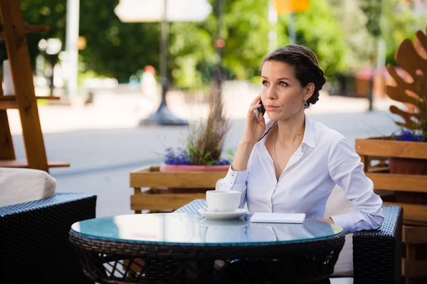 좋은 비즈니스 이야기입니다. 휴대 전화에 대 한 얘기 하 고 야외에서 앉고 있는 동안 커피의 컵을 들고 밝은 젊은 사업가 — 스톡 사진