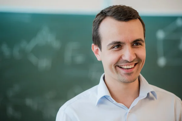 Portrait de jeune professeur souriant heureux ou étudiant homme debout près de fond tableau — Photo