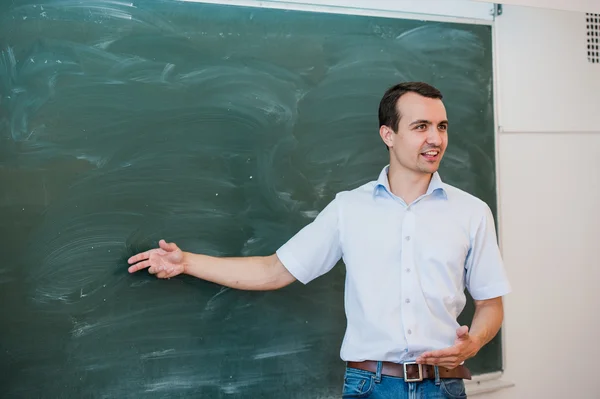 Portrait d'un jeune étudiant ou d'un enseignant beau dans une classe pointant vers un tableau blanc, parlant et souriant — Photo