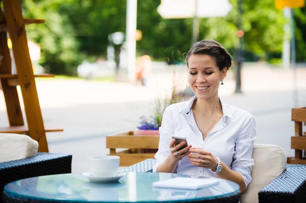 Portret uroczej kobiety biznesowej czatującej na smartfonie podczas oczekiwania kogoś w kawiarni na świeżym powietrzu, pięknej kobiety korzystającej z telefonu komórkowego podczas siedzenia w przytulnej restauracji na świeżym powietrzu podczas — Zdjęcie stockowe