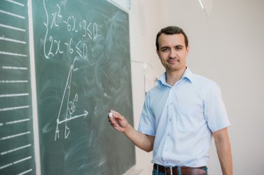 Young male teacher or student holding chalk writing on chalkboard in classroom