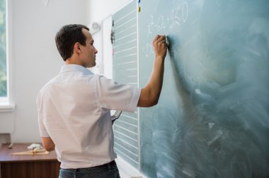 Young male teacher or student holding chalk writing on chalkboard in classroom
