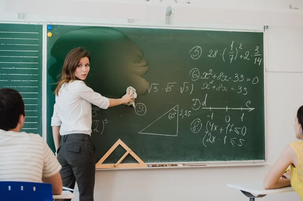 Nauczycielka w szkole myje chalkboard i lookng osób w klasie — Zdjęcie stockowe