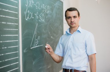 Young male teacher or student holding chalk writing on chalkboard in classroom