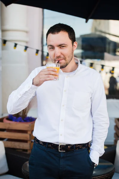 Красивий молодий чоловік тримає склянку апельсинового свіжого соку і посміхається, на відкритому повітрі — стокове фото