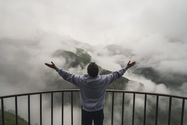 Young traveler man wearing hoodie stands on the viewpoint in national park and watching outstanding foggy landscape. Beautiful moment miracle of nature — Stock Photo, Image