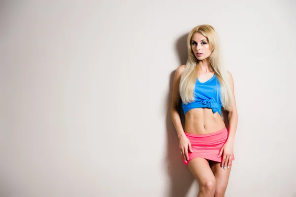 Young sport fitness sexy blonde vrouw die zich voordeed op de witte muur in blauw dank top en roze broek sneakers — Stockfoto