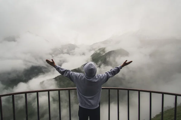 Young traveler man wearing hoodie stands on the viewpoint in national park and watching outstanding foggy landscape. Beautiful moment miracle of nature — Stock Photo, Image