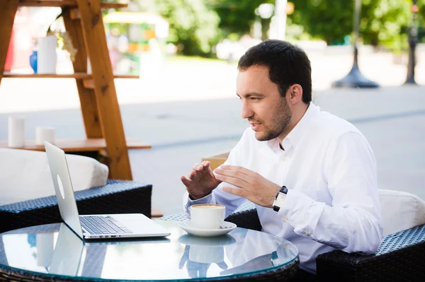 Работай и расслабься. Онлайн-конференция. Бизнесмен, одетый в рубашку, работает с ноутбуком, разговаривает по скайпу в парке кафе на открытом воздухе — стоковое фото