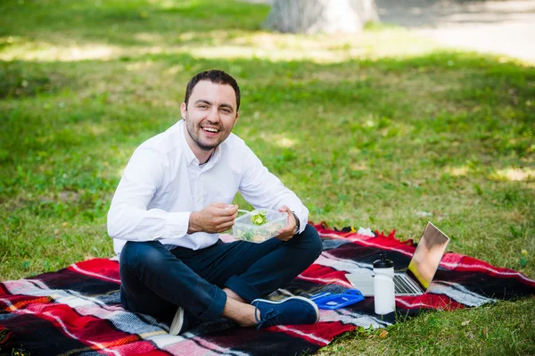 Joven hombre de negocios disfrutando de la comida que trajo en una lonchera de casa. Hora del almuerzo en el parque al aire libre . — Foto de Stock
