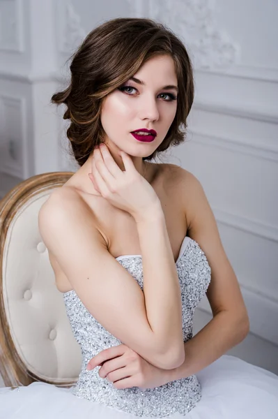 Retrato de una hermosa novia con maquillaje brillante, labios rojos sobre el interior de la habitación de lujo, sentado en la silla — Foto de Stock