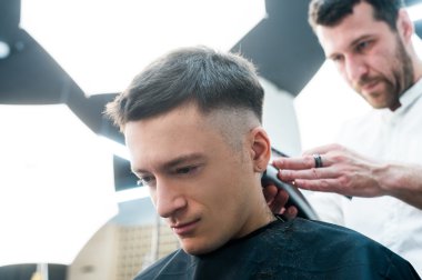 Profesyonel şekillendirme. Yan görünümü genç adamın saçını tıraş ile Kuaför tarafından berber dükkanında almak kadar kapatın