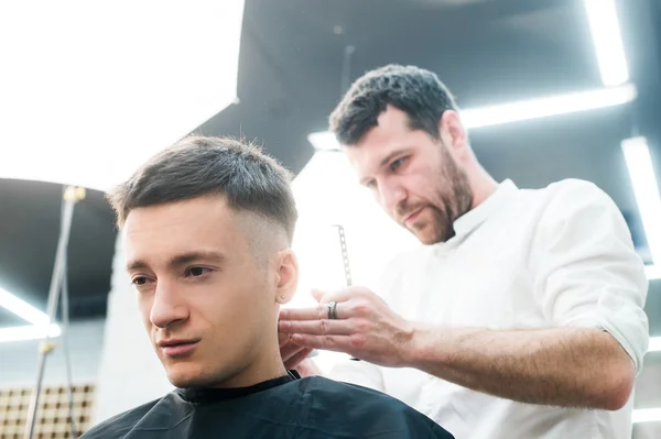 Estilo profissional. Close up vista lateral do jovem ficando corte de cabelo por cabeleireiro com navalha elétrica na barbearia — Fotografia de Stock