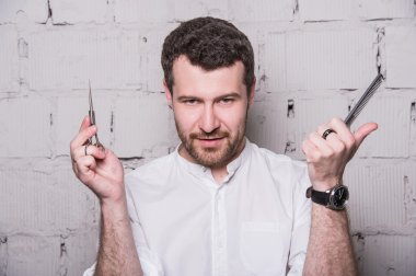 Beyaz gömlek giymiş genç Kuaför, makas ve gri tuğla duvar zemin üzerine tarak ile poz