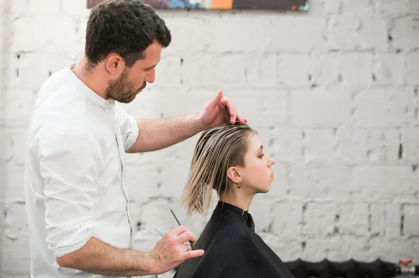 Cabeleireiro corta o cabelo com tesoura na coroa do cliente satisfeito bonito no salão de cabeleireiro profissional — Fotografia de Stock