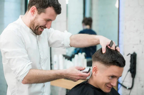 Estilo profissional. Close up vista lateral do jovem homem satisfeito recebendo corte de cabelo por cabeleireiro com navalha elétrica na barbearia — Fotografia de Stock