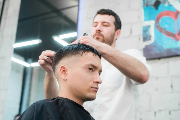 Estilo profissional. Close up vista lateral do jovem ficando corte de cabelo por cabeleireiro com navalha elétrica na barbearia — Fotografia de Stock