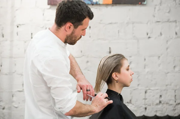Парикмахер стрижет ножницами волосы на короне красивого довольного клиента в профессиональном парикмахерском салоне — стоковое фото