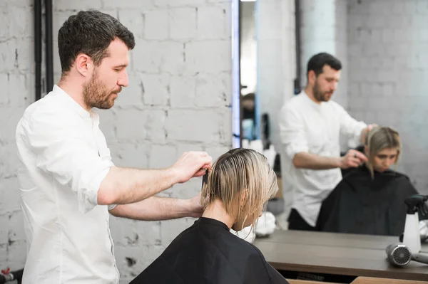 Cabeleireiro corta o cabelo com tesoura na coroa do cliente satisfeito bonito no salão de cabeleireiro profissional — Fotografia de Stock