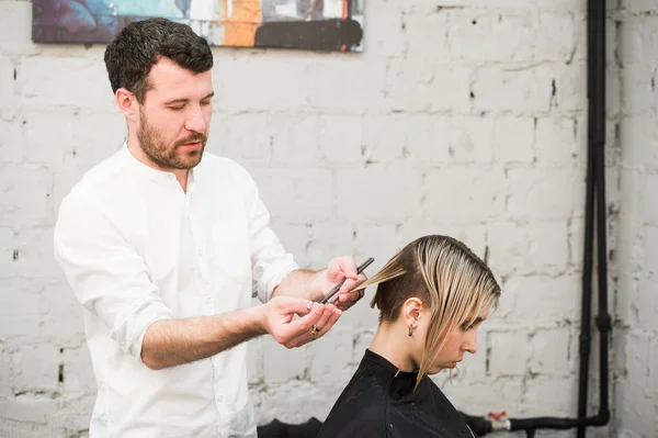 Парикмахер стрижет ножницами волосы на короне красивого довольного клиента в профессиональном парикмахерском салоне — стоковое фото