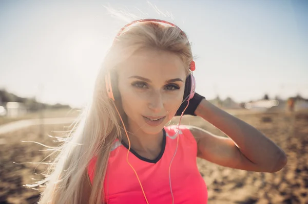 Portret młodej kobiety pięknej, słuchania muzyki na plaży. Bliska twarz uśmiechający się blondynka z słuchawki patrząc na kamery. Dziewczyna, działa na plaży i słuchania muzyki. — Zdjęcie stockowe