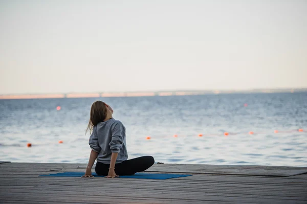 Morning shot of a girl in lotus position doing stretching yoga exercises on the pier — Stock Photo, Image