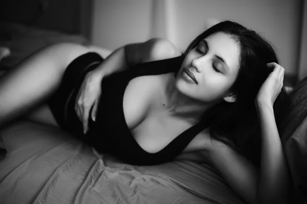 Mulher morena muito sexy deitada na cama vestindo roupa interior preta. Acorde erótico, imagem monocromática — Fotografia de Stock