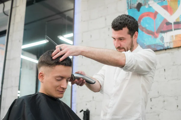 Estilo profissional. Close up vista lateral do jovem homem satisfeito recebendo corte de cabelo por cabeleireiro com navalha elétrica na barbearia — Fotografia de Stock