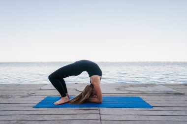 Güzel sportif fit siyah spor sarışın genç kadın göl üzerinde ahşap duon üzerinde açık havada çalışma, Köprü Pose yapıyor, Urdhva Dhanurasana ayakta, Chakrasana duruş, tam uzunlukta
