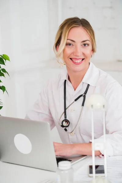 Retrato de una joven doctora con estetoscopio en bata blanca en la computadora — Foto de Stock