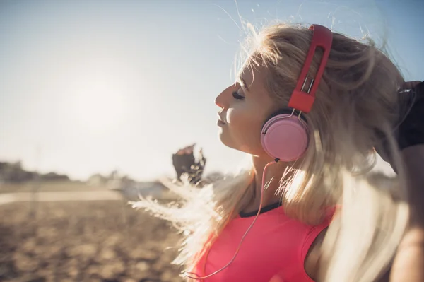 Portrait of young beautiful woman listening to music at beach. Close up face of smiling blonde woman with earphone looking at camera. Girl running at beach and listening to music.