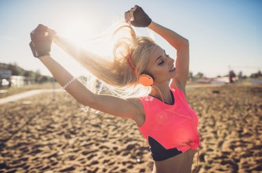 Plajı'nda müzik dinlemek genç güzel kadın portresi. Gülümseyen sarışın kadın yüzünü kameraya bakarak kulaklık ile kapatın. Kumsalda çalıştıran ve müzik kız.